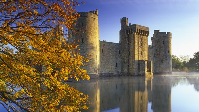 A slight mist rises from the moat at dawn at 14th-century Bodiam Castle, East Sussex. The moat reflects the castle along with golden leaves in the foreground